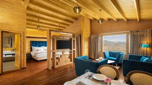 A spacious room with a wooden ceiling, a large bed, a television, and a dining area with blue chairs and a table set for two. -  juSTa Cliffend Resort & Spa Mashobra Shimla (Shimla)