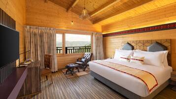 A wooden cabin room with a large bed, a desk, and a chair.