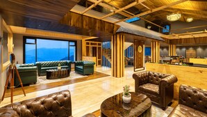 A spacious lobby with leather sofas, a wooden reception desk, and a large window offering a view of the mountains. -  juSTa Cliffend Resort & Spa Mashobra Shimla (Shimla)
