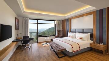 A modern hotel room with a large bed, a desk, and a view of the mountains.