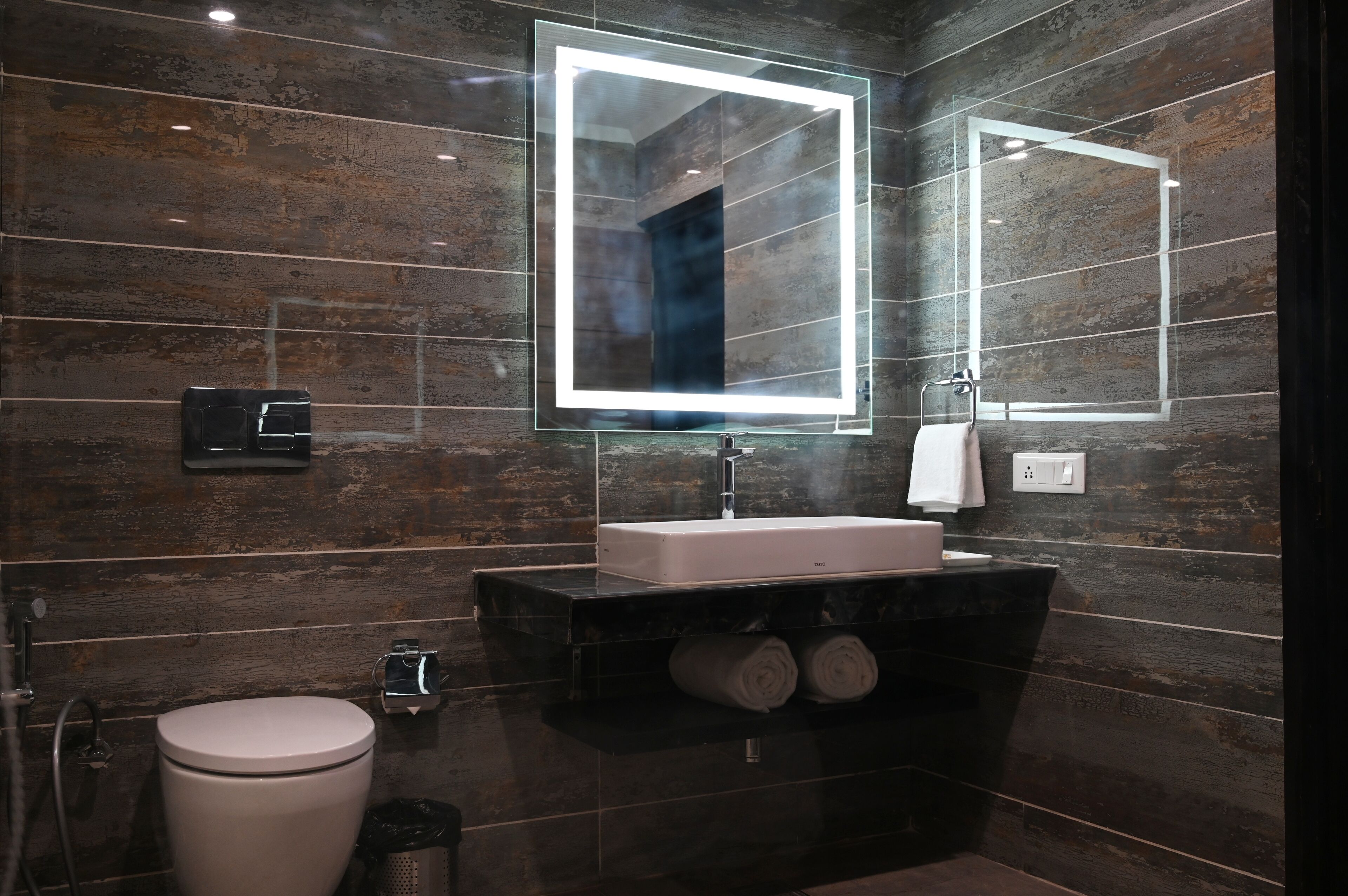A modern bathroom with a large mirror, a white sink, and a toilet.