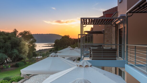 Eine Terrasse mit Sonnenschirmen, einer Steinmauer und Blick auf das Meer im Sonnenuntergang.