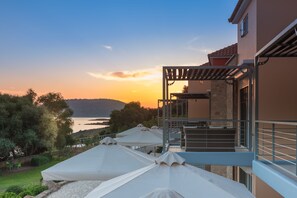 A terrace with umbrellas, a stone wall, and a view of the sea at sunset.