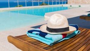 Eine Liege mit Hut und Handtüchern an einem Pool mit Meerblick.
