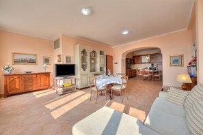 A spacious living area with a sofa, TV, dining table, and kitchen in the background. - Angela -terrace & Beautiful View Lake (Toscolano Maderno)