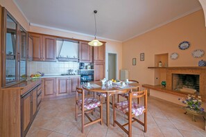 A kitchen with wooden cabinets, a dining table with chairs, a hanging light fixture, and a fireplace. - Angela -terrace & Beautiful View Lake (Toscolano Maderno)