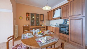 Une cuisine avec des meubles de rangement en bois, une table à manger dressée avec des assiettes, des tasses et un panier de fruits.