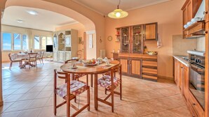Une cuisine spacieuse avec des meubles en bois, un coin repas doté d’une table ronde, et une vue sur une autre pièce accessible par une arche.