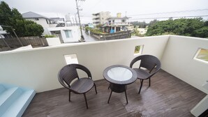 Een balkon met twee rieten stoelen, een klein rond tafeltje, een blauwe bank en een paar schoenen.