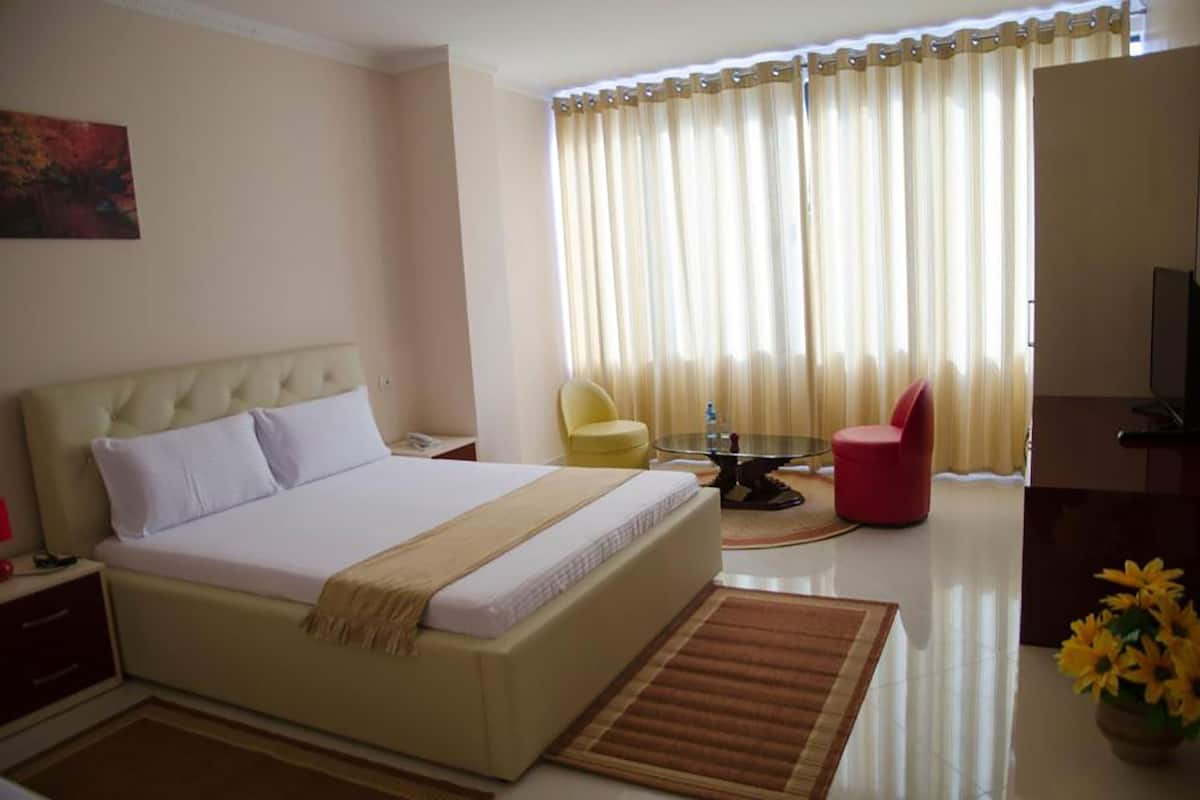 A hotel room with a bed, a chair, a TV, and a window with curtains.