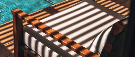 A wooden chair with a cushioned seat and backrest, positioned near a pool with a metal ladder.