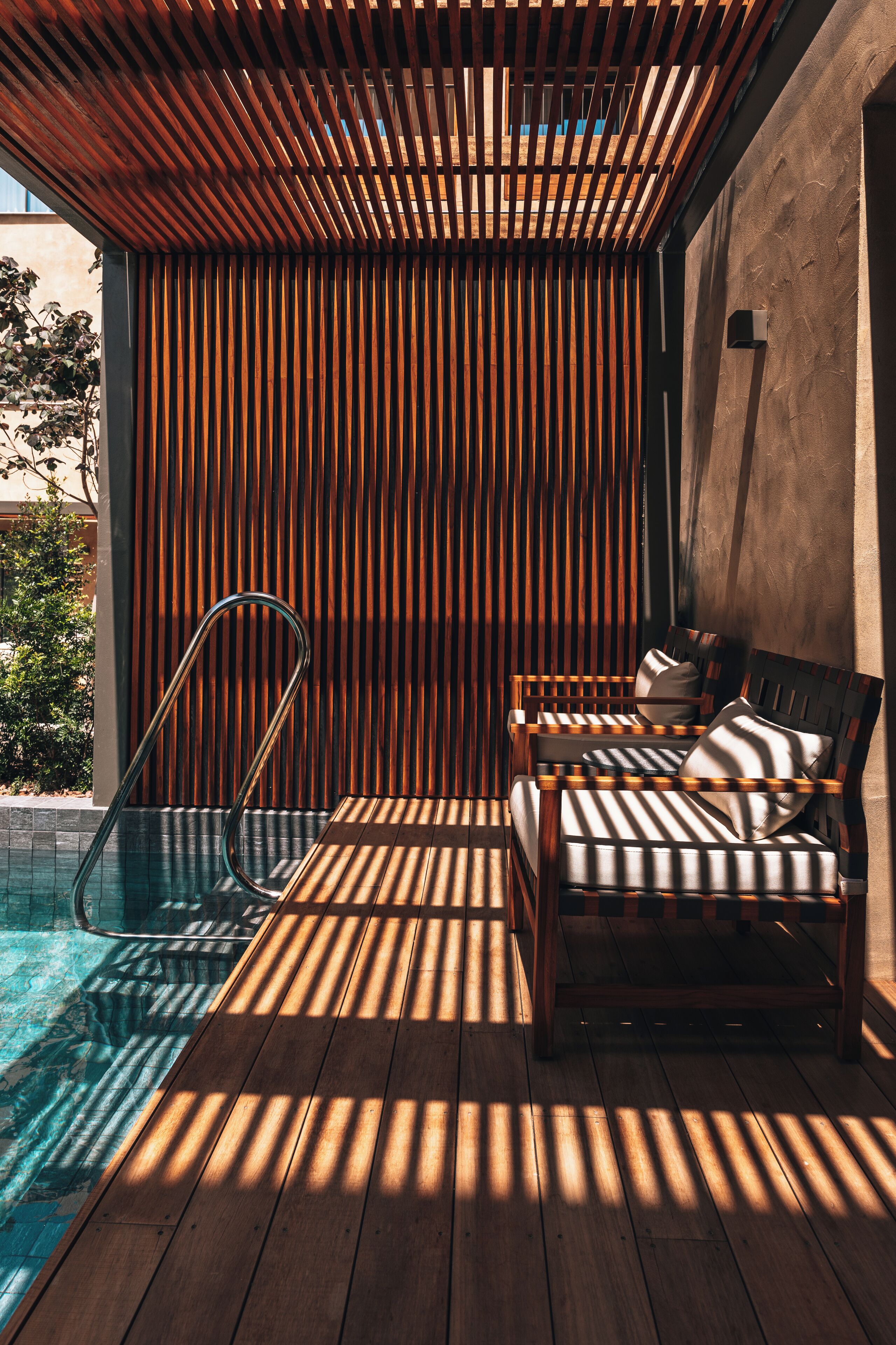 A wooden deck with a pool, a lounge chair, and a wooden slatted wall.