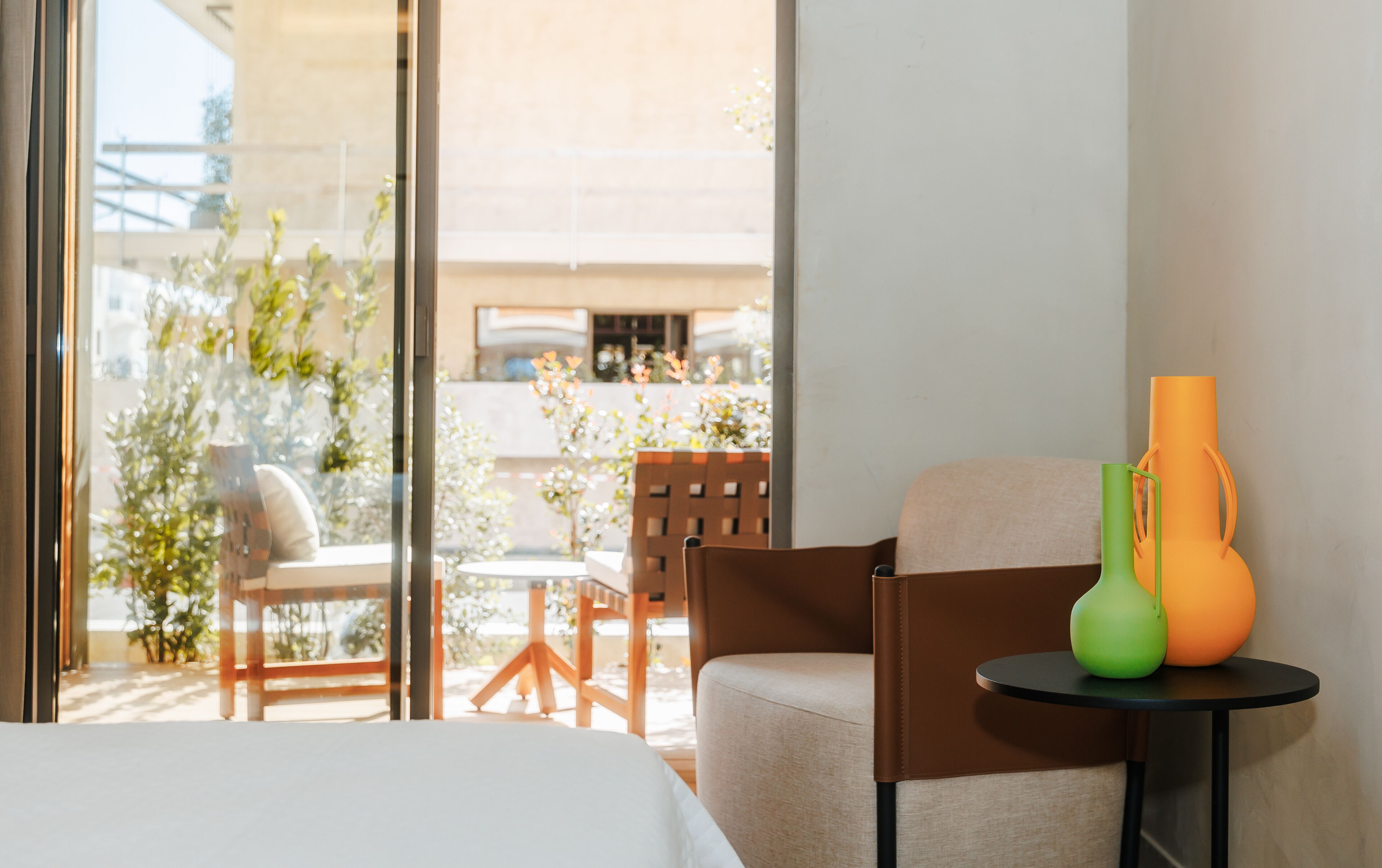 A hotel room with a bed, a chair, a small table, and a vase.