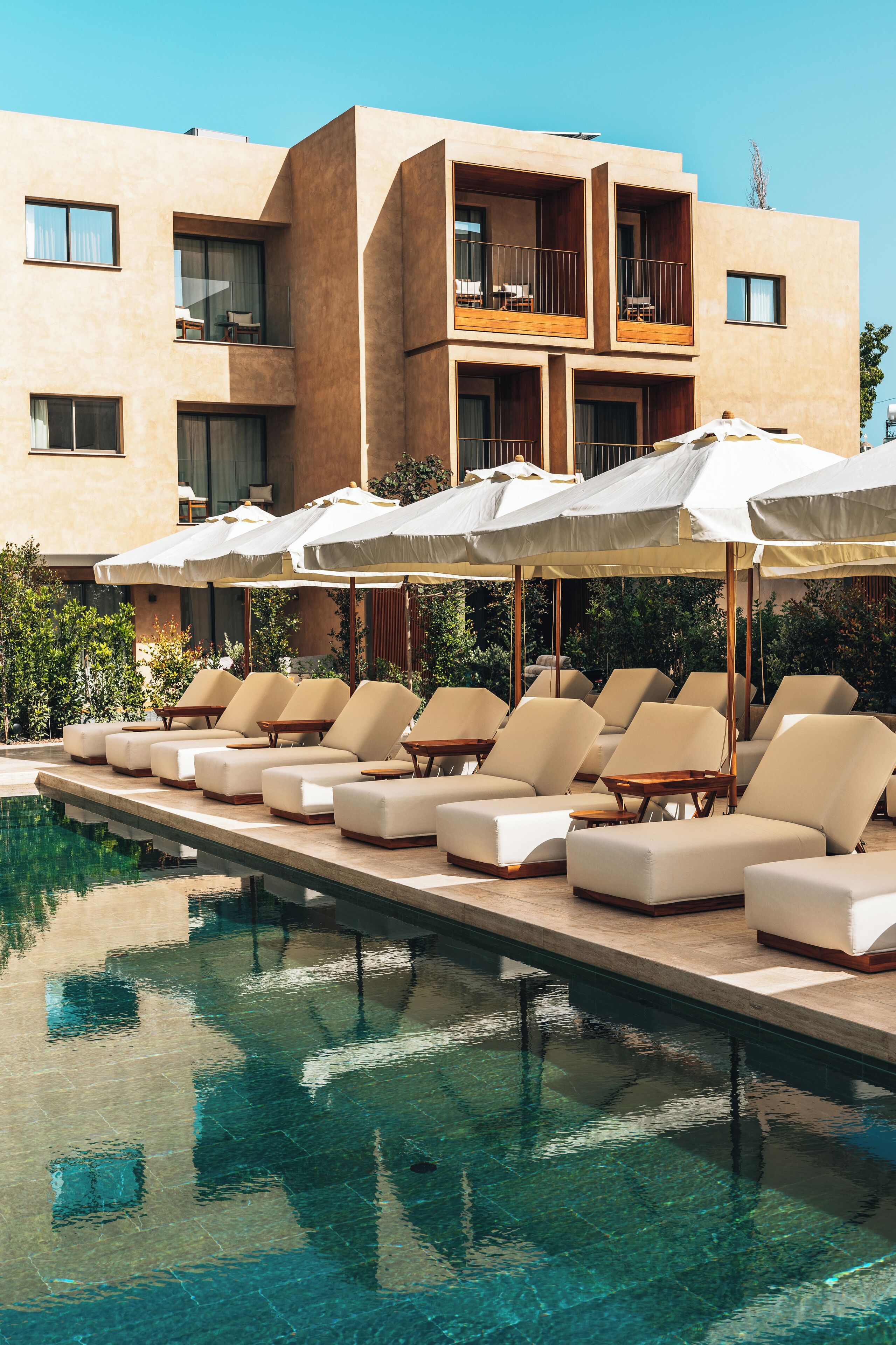 A poolside area with lounge chairs and umbrellas, a clear pool, and a building with balconies.