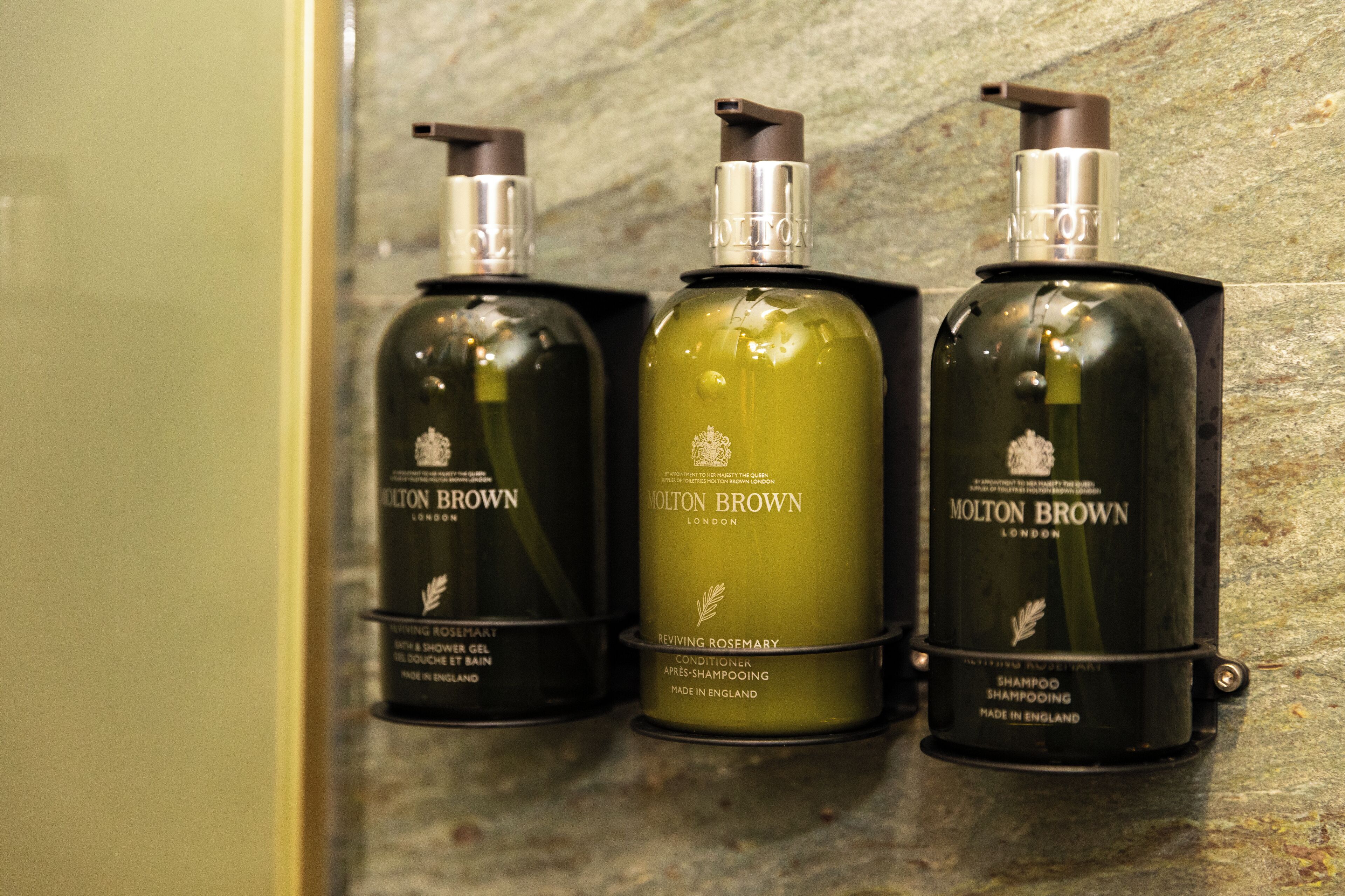 Three bottles of Molton Brown products on a textured wall.