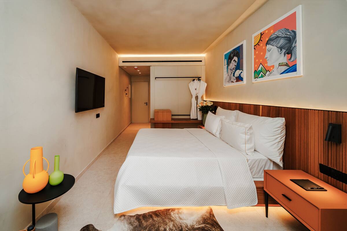 A modern hotel room with a large bed, a bedside table, a flat-screen TV, and artwork on the walls.