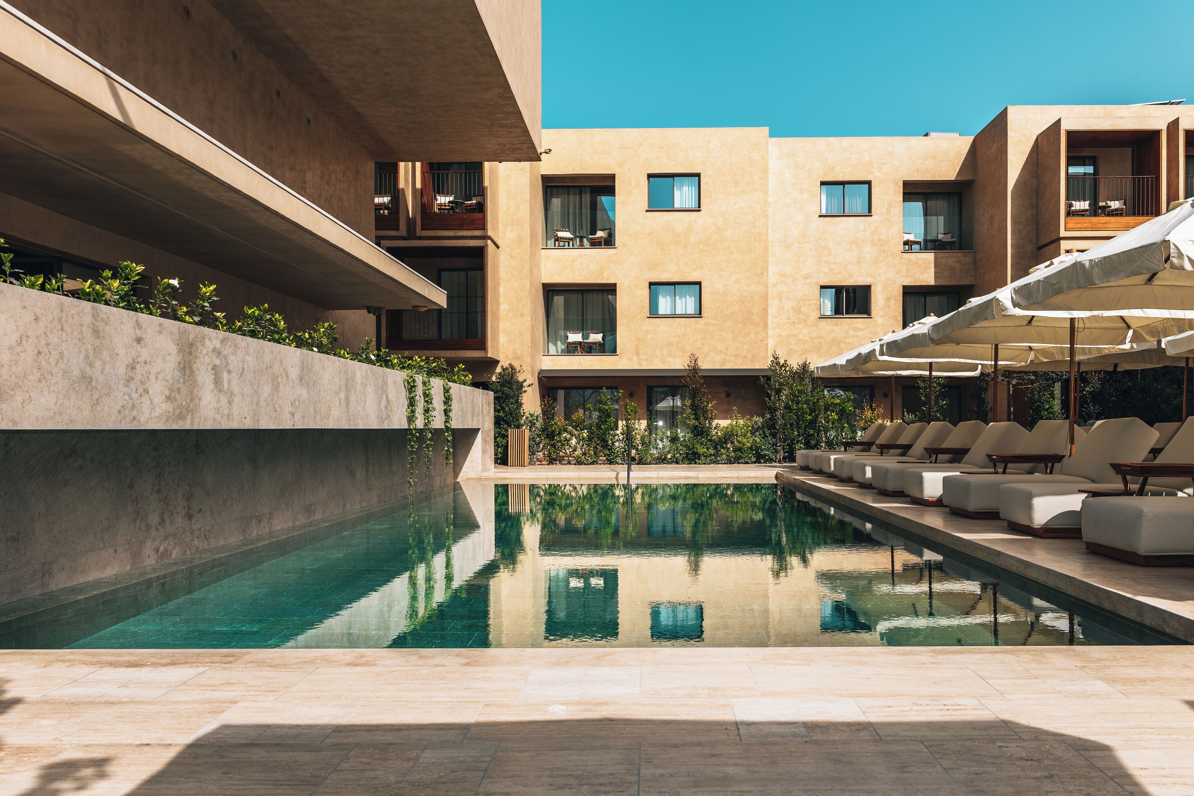 Un espace piscine moderne, doté de chaises longues et offrant une vue dégagée sur la façade du bâtiment.