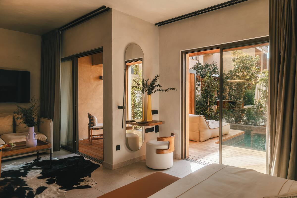 A modern bedroom with a large bed, a glass door leading to a balcony with a pool, and a minimalist decor.