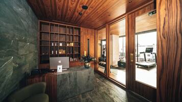 A reception area with a wooden reception desk, a computer, a plant, and a view of a gym.