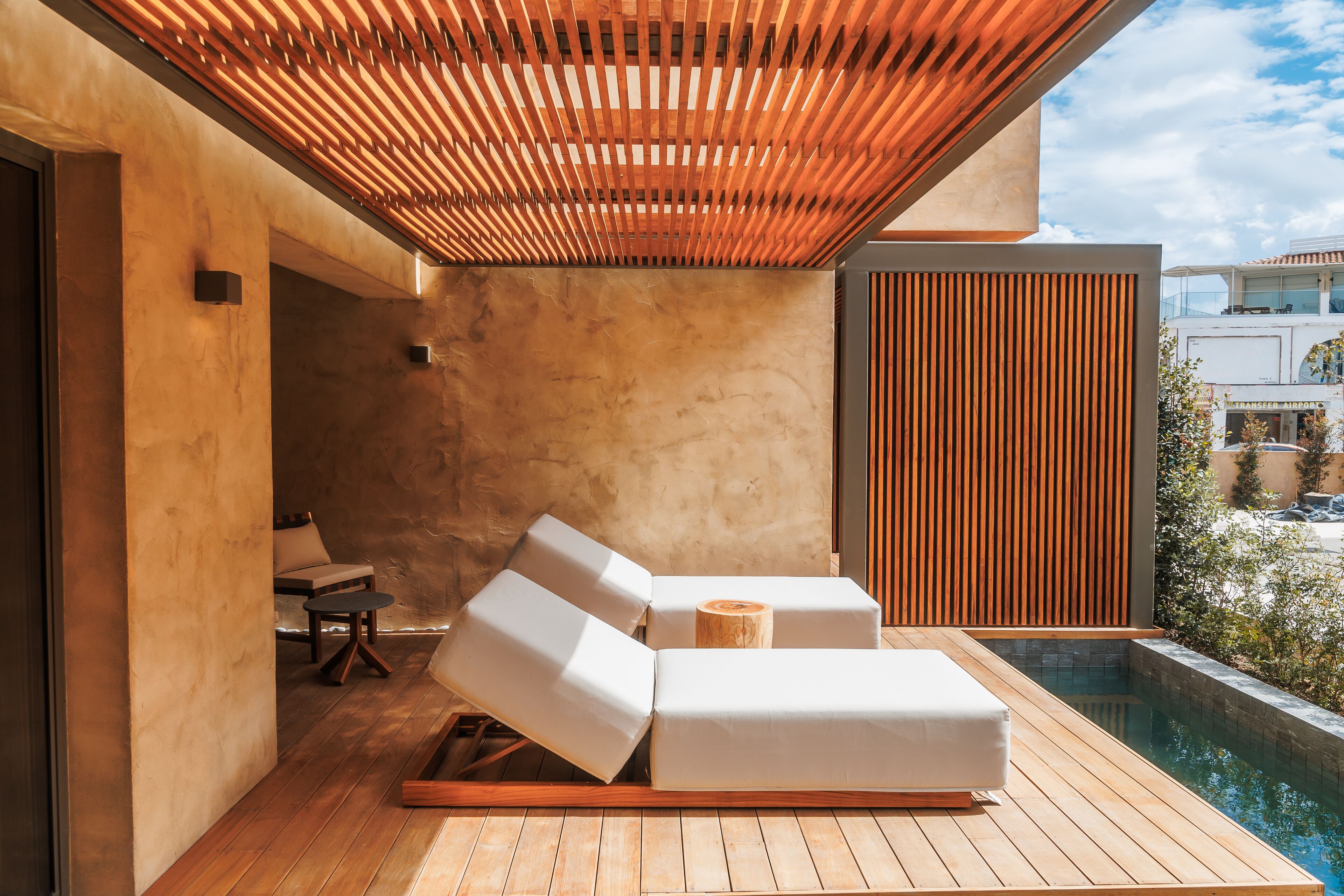 A modern outdoor lounge area with wooden flooring, two white lounge chairs, a small round table, and a wooden stool.
