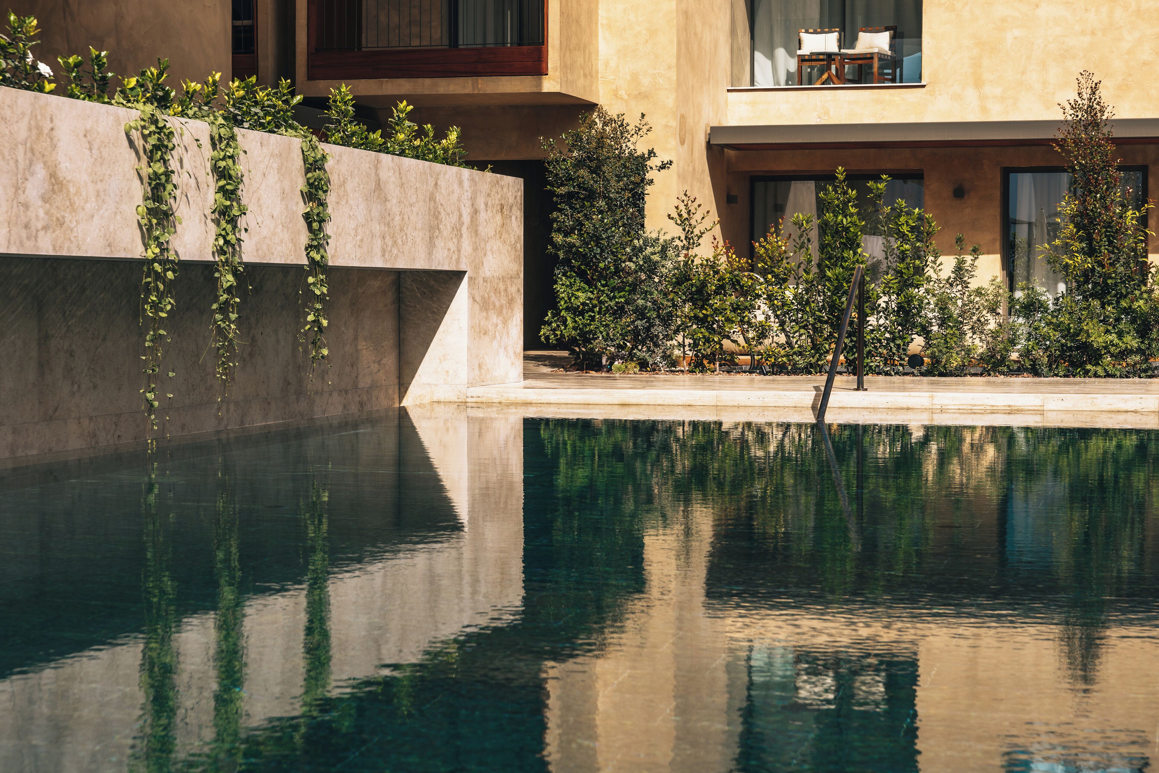 Une piscine à l’eau claire, dont la surface reflète la végétation environnante, et un bâtiment au design moderne.