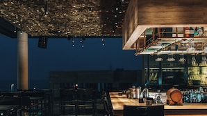 A bar area with wooden flooring, metal chairs, and a bar counter with various bottles and glasses. - M Boutique Hotel - Designed for Adults (Paphos)