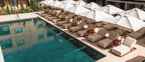 A poolside area with lounge chairs and umbrellas, a clear pool, and a building with large windows in the background.
