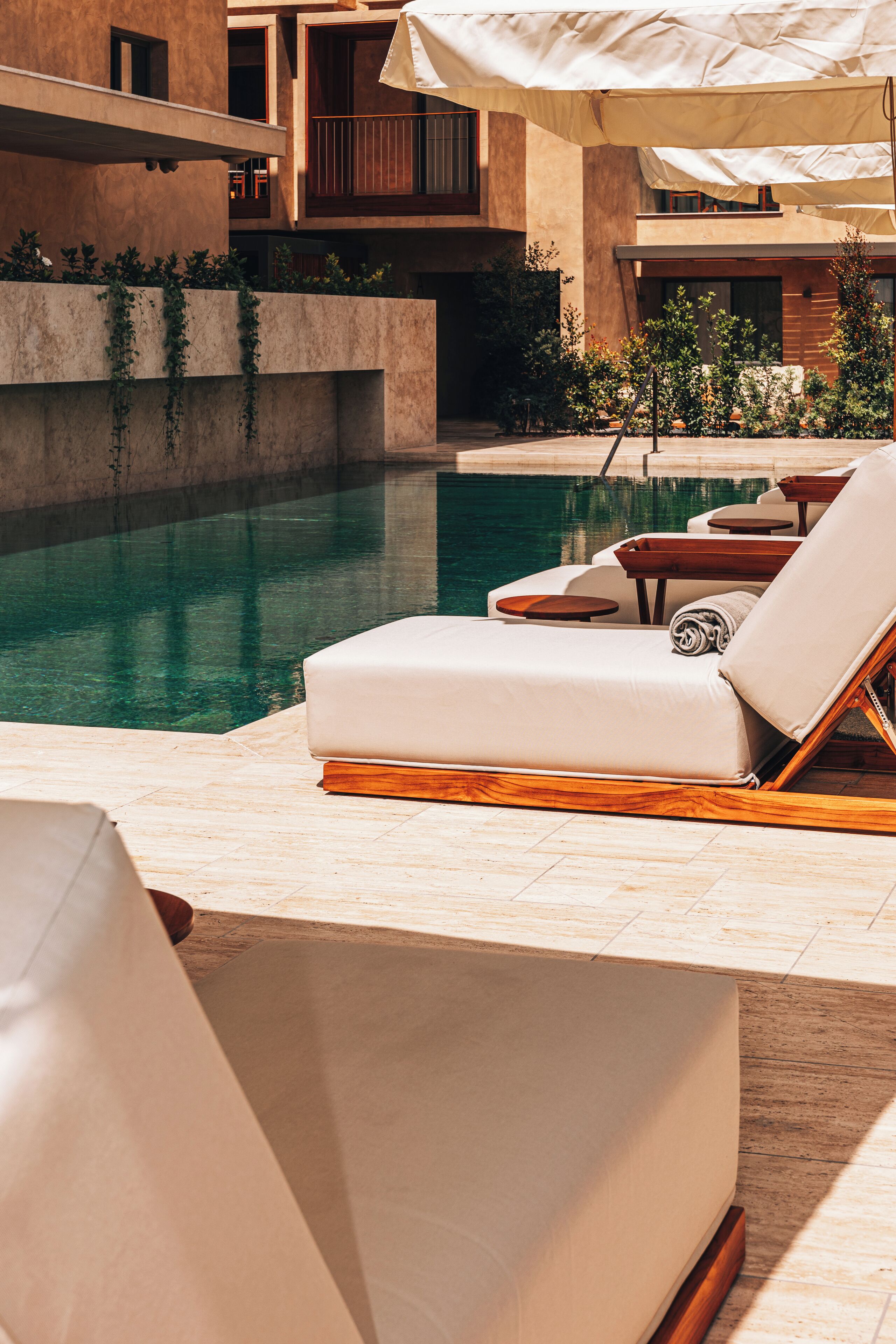 A poolside area with lounge chairs and umbrellas, a clear pool, and a building with balconies.