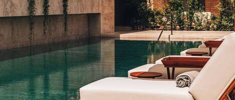 A poolside area with lounge chairs and umbrellas, a clear pool, and a building with balconies.