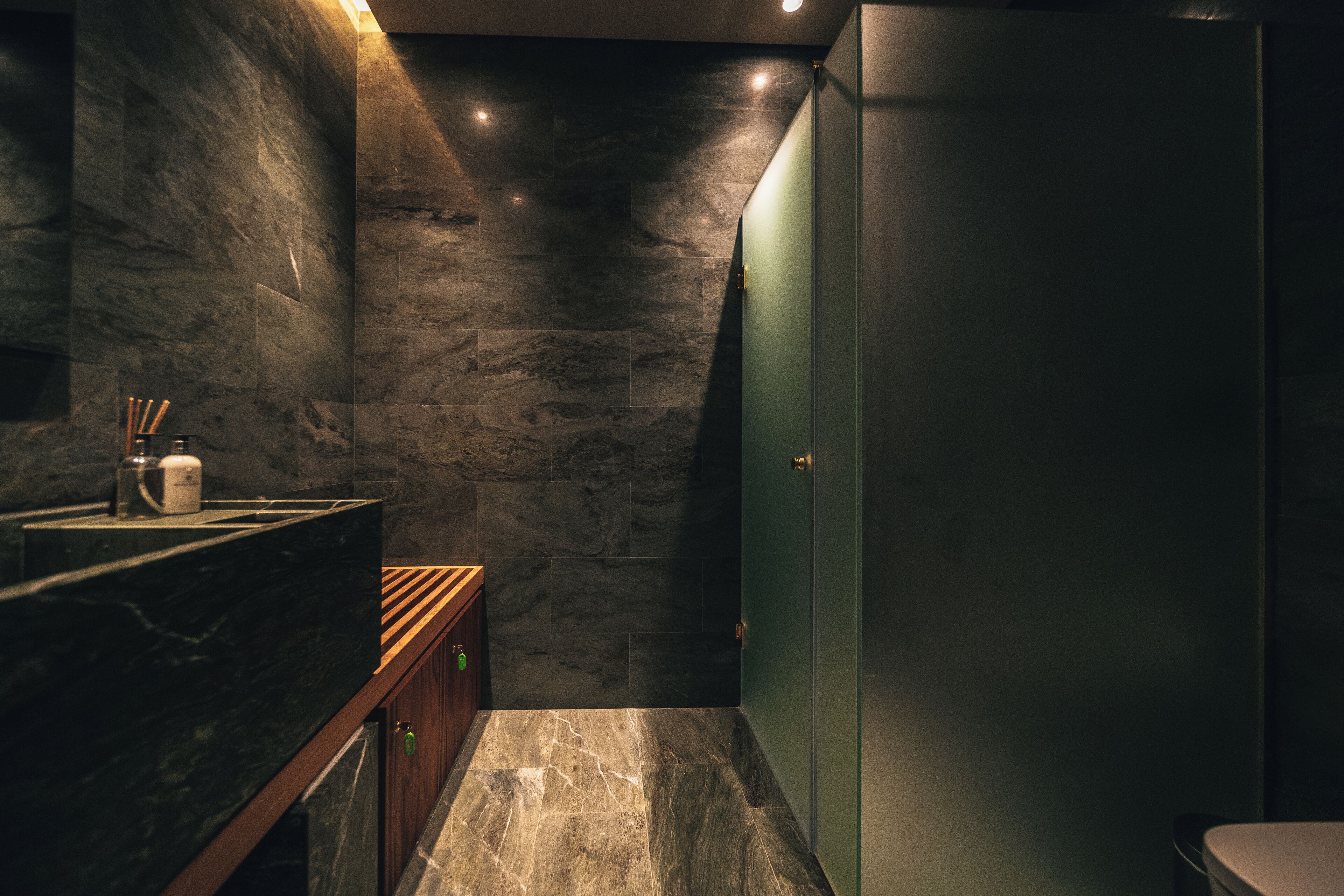 A modern bathroom with a marble countertop, wooden cabinet, and a green door.