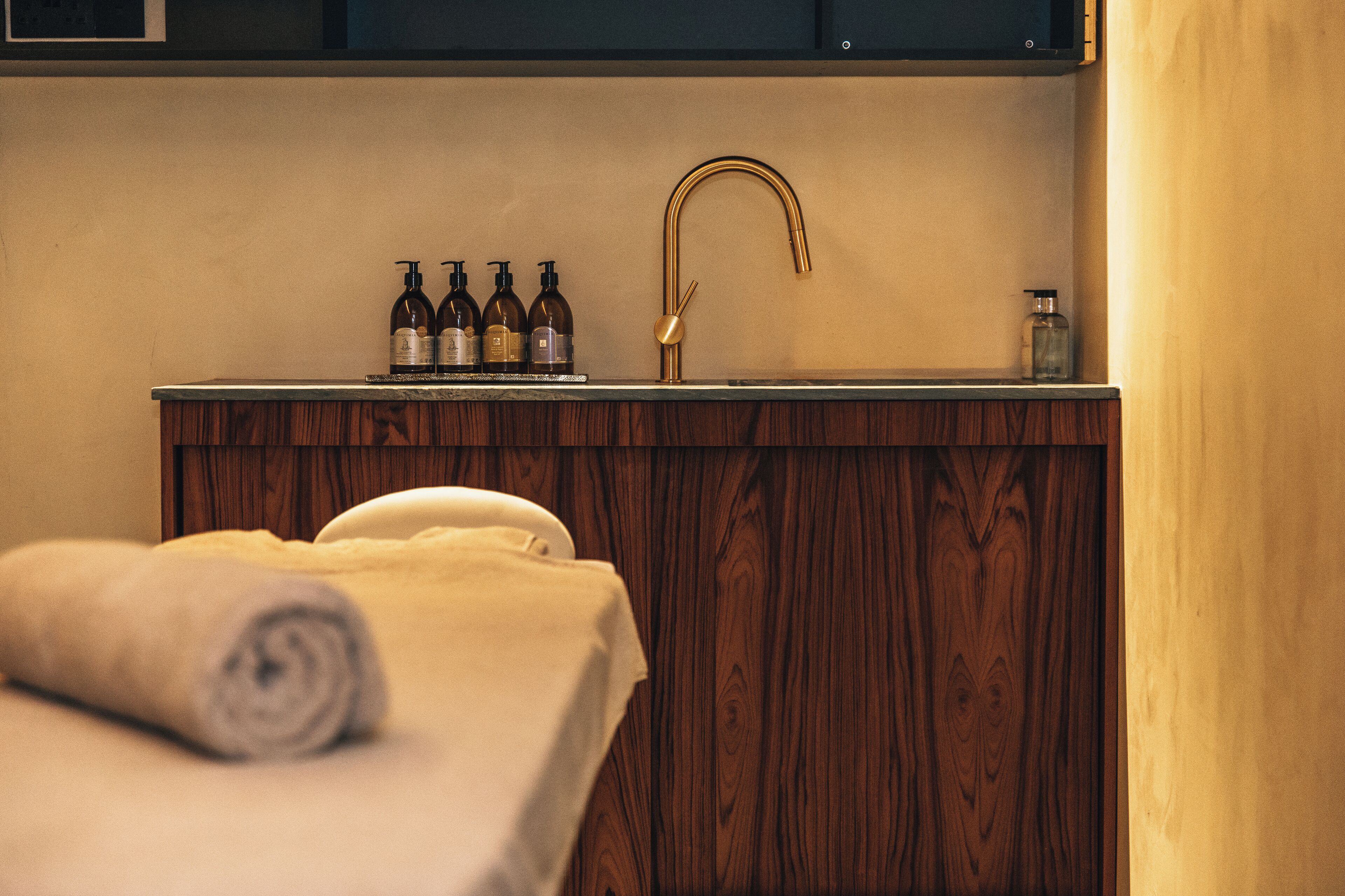 Une coiffeuse en bois avec un lavabo, des flacons et une serviette.