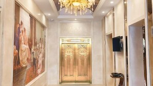 A hallway with a large painting on the left, a chandelier, and an ornate elevator. - Vienna International Hotel (Liupanshui Shuicheng) (Liupanshui)