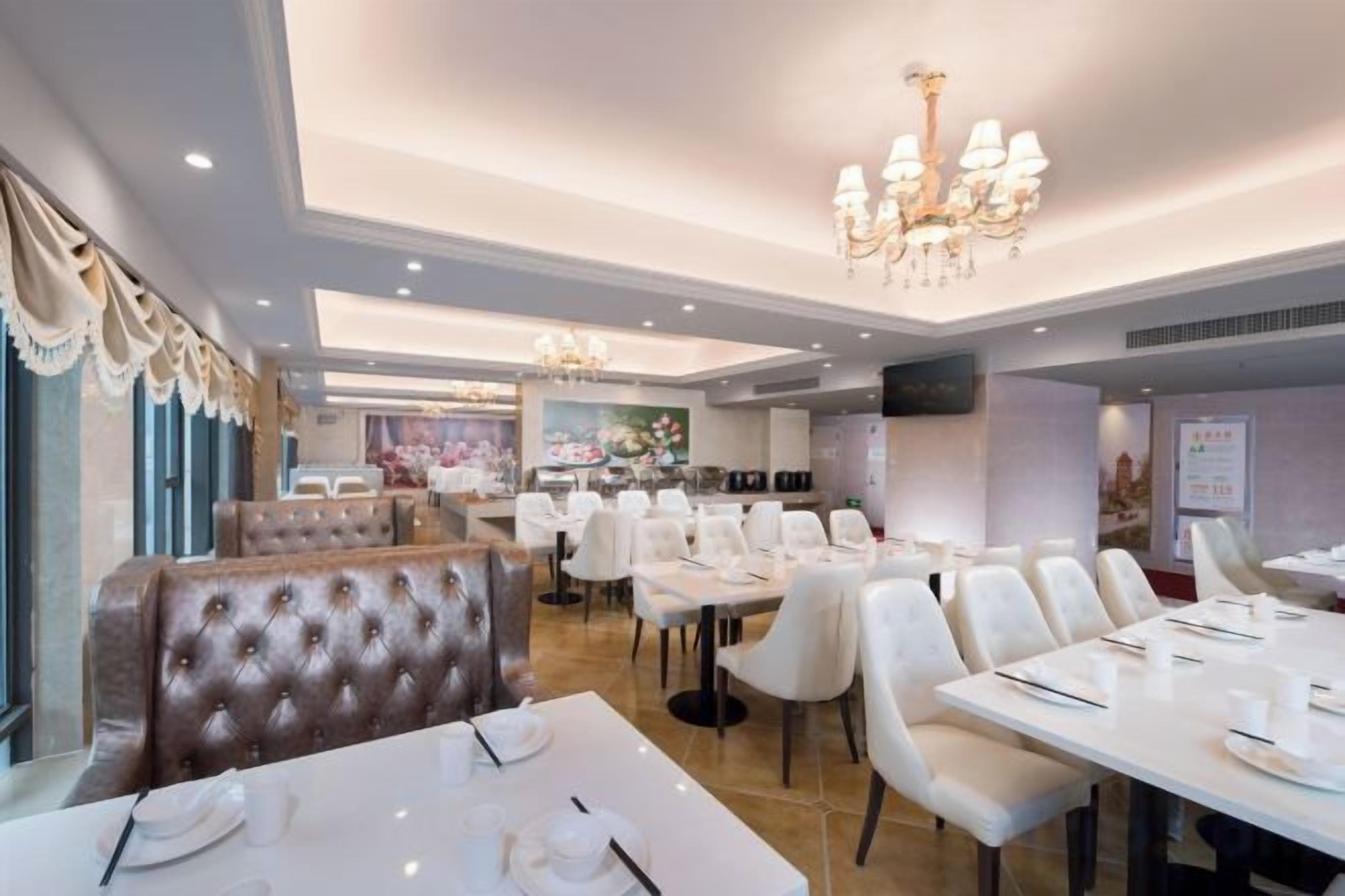A restaurant with white table settings, a chandelier, and a large window with curtains.
