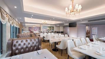 A restaurant with white table settings, a chandelier, and a large window with curtains.