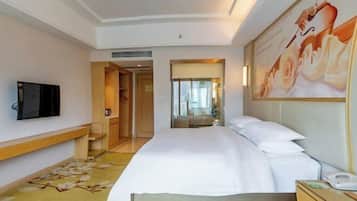 A hotel room with a bed, a TV, a desk, and a painting on the wall.