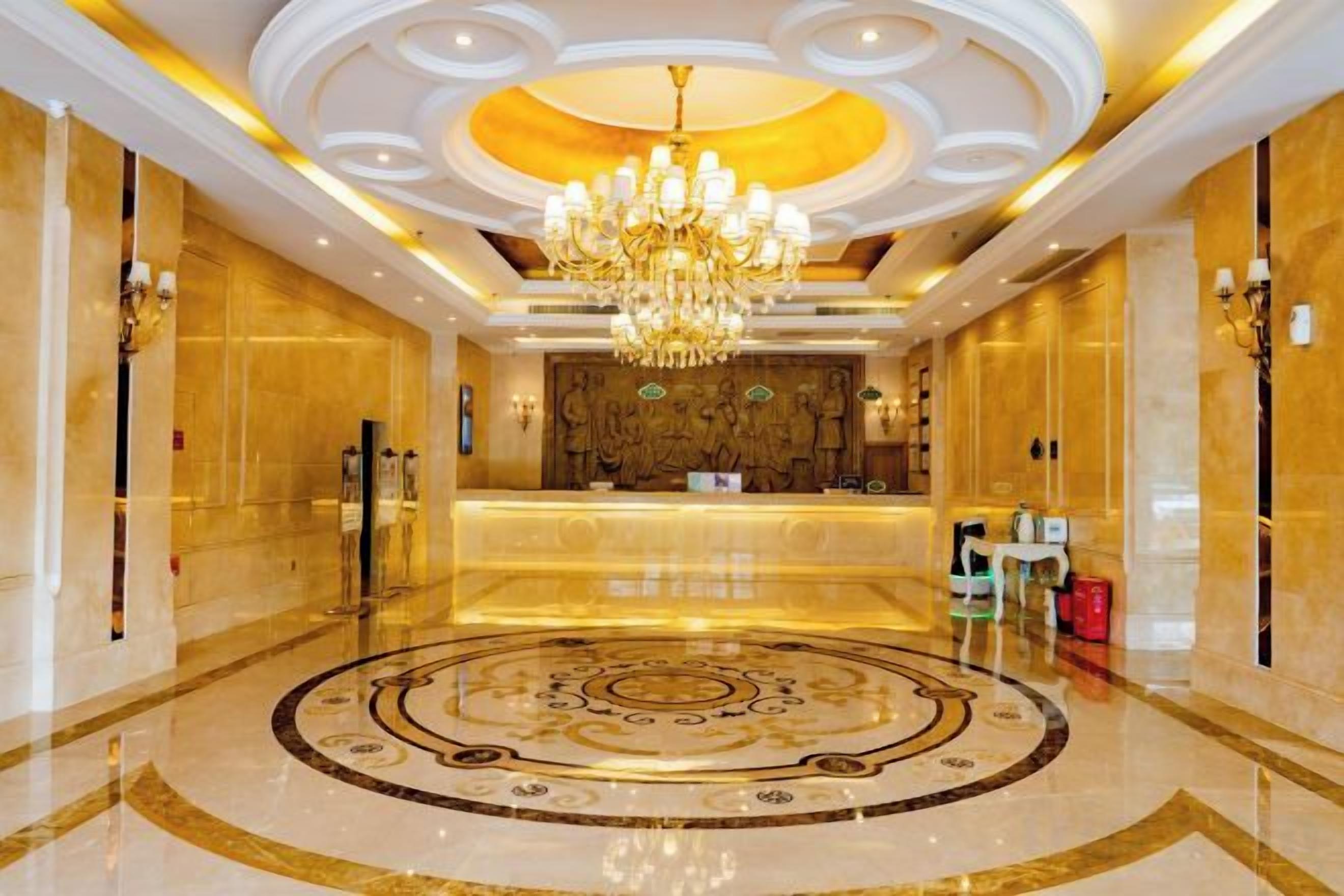 A hotel lobby with a central reception desk, a chandelier, and a circular patterned floor.