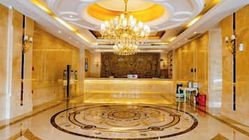 A hotel lobby with a central reception desk, a chandelier, and a circular patterned floor.