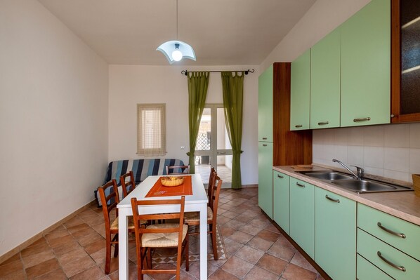 A compact kitchen with a dining area, green cabinets, a white table, and a window with curtains.