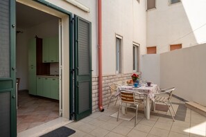 An open door leading to a kitchen with green cabinets, a dining table with chairs, and a red pipe on the wall.