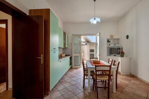 A kitchen with a dining table, chairs, a refrigerator, cabinets, and a hanging light fixture.