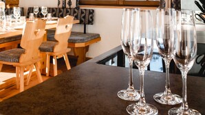 Un coin repas avec des chaises en bois et une table, une fenêtre avec des rideaux et un espace cuisine équipé d’une cuisinière.