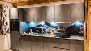 Et moderne køkken med grå skabe, en rustfri stålvask og et backsplash med et bjergmotiv.