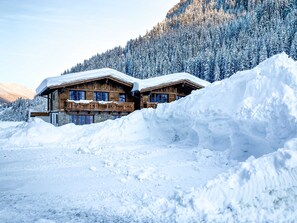 A wooden chalet with a stone foundation, surrounded by snow and forested mountains. - Stadl-suite Silvretta - Stadl Chalet Ischgl (Ischgl)
