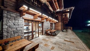 Un bâtiment en pierre avec des poutres en bois, un patio avec des bancs et un éclairage extérieur soigné.