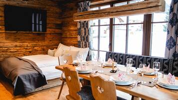 Une cabane en bois avec un lit, une table à manger dressée pour quatre personnes et une grande fenêtre.