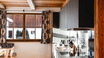Eine moderne Küche mit Holzbalkendecke, einem Essbereich mit Stühlen und einem großen Fenster mit Vorhängen.