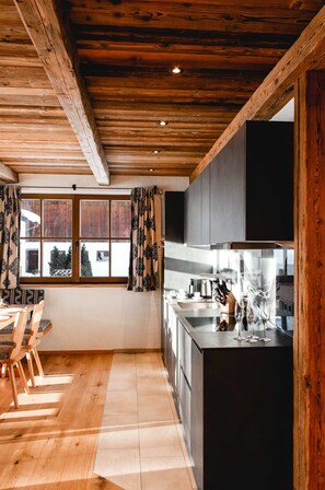 Uma cozinha moderna com vigas de madeira no teto, uma área de jantar com cadeiras e uma janela grande com cortinas.