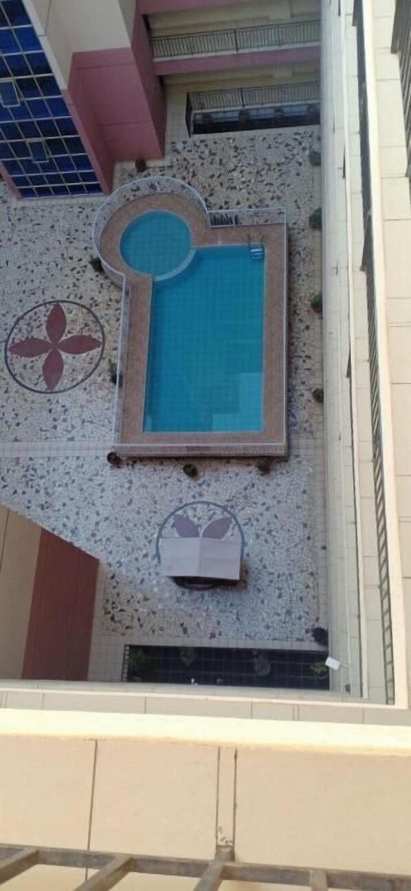 A rooftop pool area with a rectangular pool, a circular hot tub, and a decorative tile design.