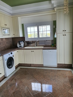 A kitchen with a washing machine, dishwasher, and a window with a view of greenery.