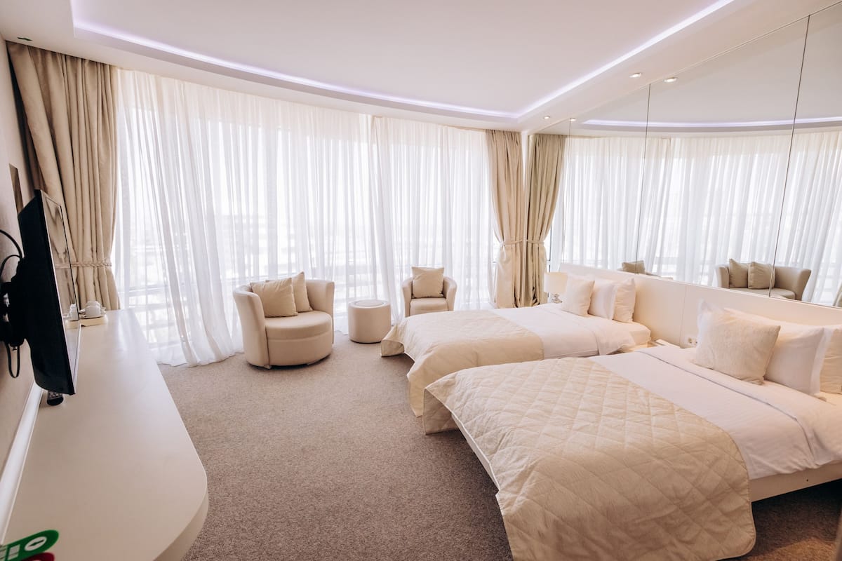 A hotel room with two beds, a sofa, a TV, and a large window with curtains.